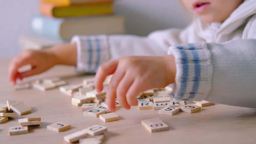 hands close-up, small child 3 years old plays wooden alphabet blocks, makes up words from letters, dyslexia awareness, learning difficulties, human brain development, happy childhood, selective focus