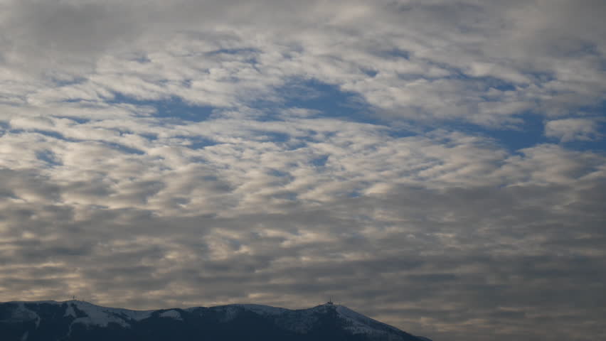 fast moving clouds in the sky over the snowy mountain with snow on top in the morning, time lapse video