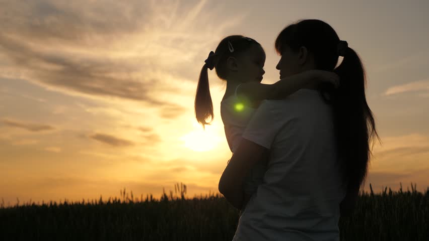 Mom and child daughter are walking on field, sunset. Child girl hugging mom outdoors. Happy family mother, daughter in field at sunset. Farmer mother, child. Happy family, nature. Mom, kid silhouette