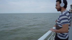 4k video of a young latin man wearing headphones looking at the ocean from the deck of a ferry. Copy space.