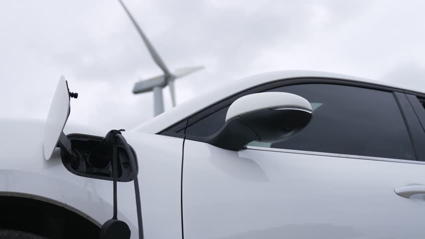 Progressive future energy infrastructure concept of electric vehicle being charged at charging station powered by green and renewable energy from a wind turbine in order to preserve the environment. | Shutterstock HD Video #1100963651