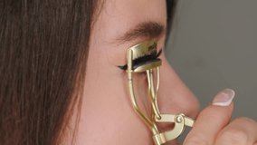 Young woman curls eyelashes using special beauty equipment. Lady takes care of lashes before applying makeup on grey background extreme closeup - Powered by Shutterstock - Get 15% off with code: PIKWIZARD15