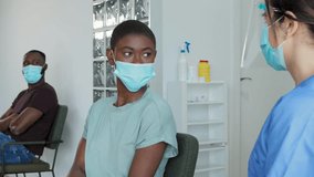 Female medical specialist in protective uniform, latex gloves and face shied vaccinating African American female patient with in clinic office during coronavirus outbreak. Real time 4k video