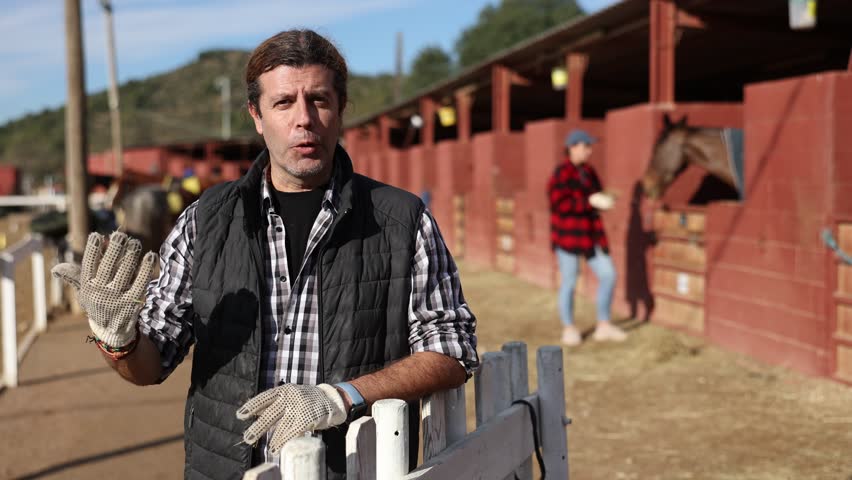 Owner of the stable poses talking in front of the corral for horses 