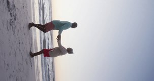 Vertical video of senior african american couple dancing at beach, in slow motion. Spending quality time, lifestyle, retirement and holiday concept.