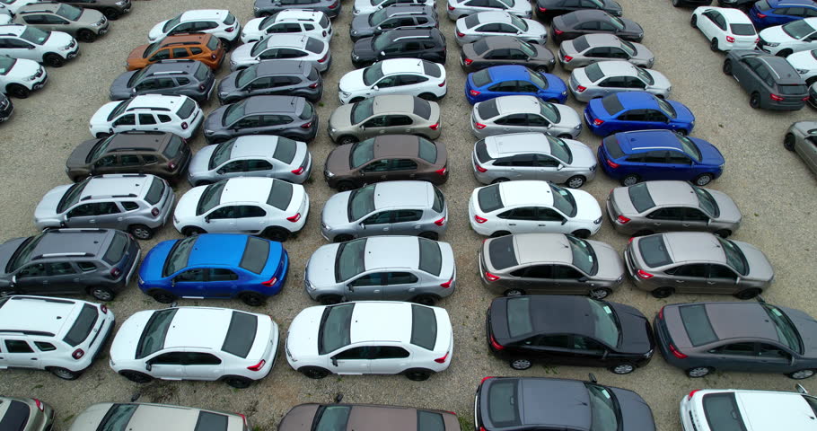 Densely parked to each other cars in the parking lot of the car market. Aerial shot. Multi-colored cars in the parking lot of the warehouse.