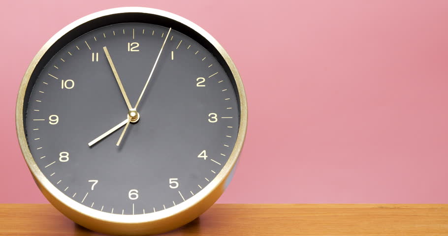 Black desk clock inlaid with gold frame is placed on the wooden floor with a pink background and a walking time of 7:53 AM.