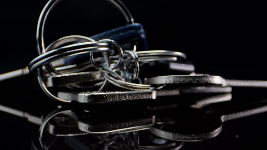 A bunch of keys lies on a black mirror surface and spins slowly. Macro shot Royalty-Free Stock Footage #1100982519