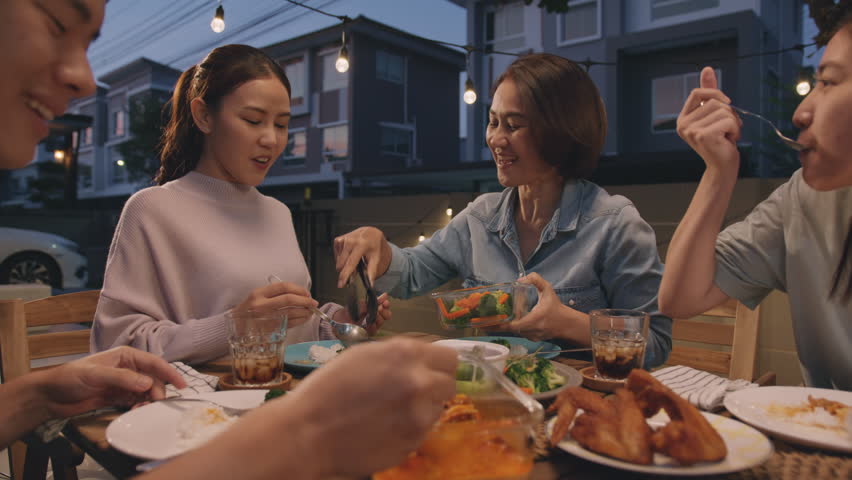 Mom enjoy thai meal cooking for family day home dining at dine table cozy patio. Mum passing serving food to group four asia people young adult man woman friend fun joy relax warm night picnic eating. | Shutterstock HD Video #1100983423