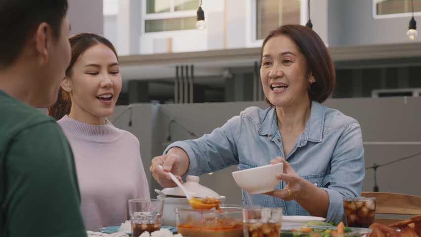 Mom enjoy thai meal cooking for family day home dining at dine table cozy patio. Mum passing serving food to group four asia people young adult man woman friend fun joy relax warm night picnic eating. | Shutterstock HD Video #1100983427