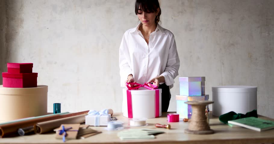 Woman standing at table tying ribbon around gift box