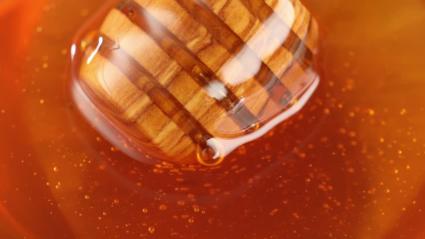 Honey dripping from honey dipper in glass bowl. Close-up. Healthy organic Thick honey dipping from the wooden honey spoon, closeup. jar on the wood table. organic food on color background.