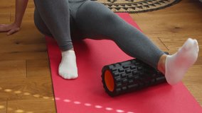 Sport female in grey leggings doing exercises on foam roller for warm up, massage calf muscle on wooden floor in room indoors. Workout to remove pain in leg at home. Rehabilitation in sports medicine - Powered by Shutterstock - Get 15% off with code: PIKWIZARD15