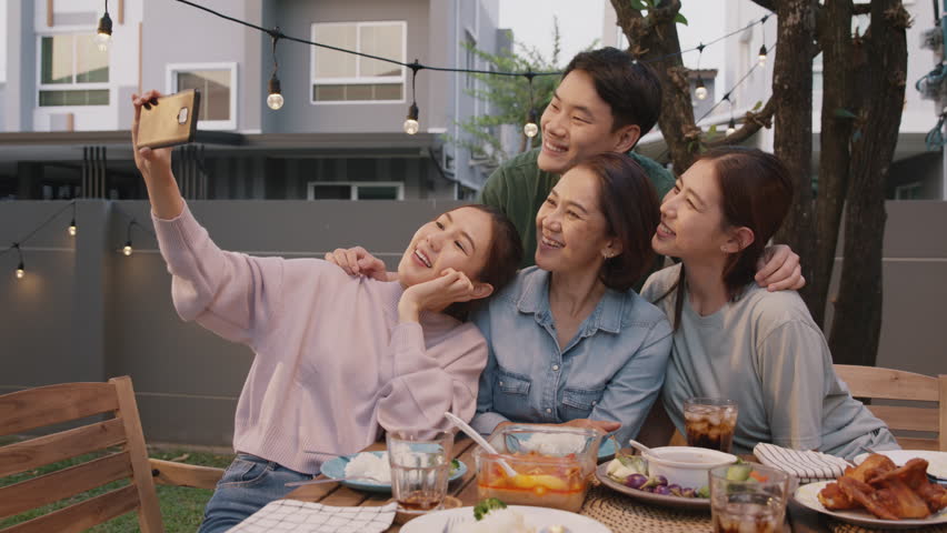 Young adult asia people hug love care for mom taking photo selfie video on mobile phone camera at home picnic dining fun night party dine table. Relax older mum smile enjoy warm time happy hour meal. | Shutterstock HD Video #1100988767