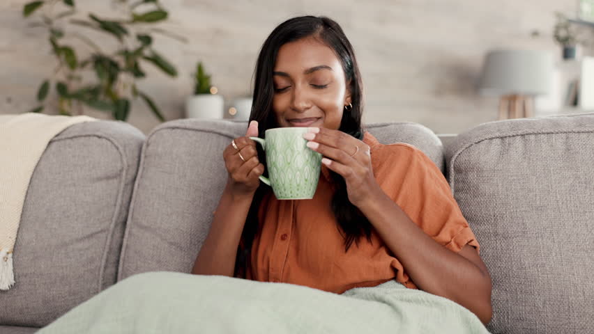 Relax, coffee and Indian woman on couch, peace and resting on break, happiness and calm in living room. Female, tea or happy lady with smile, joyful or gratitude with natural aroma, sofa or self care Royalty-Free Stock Footage #1100989341