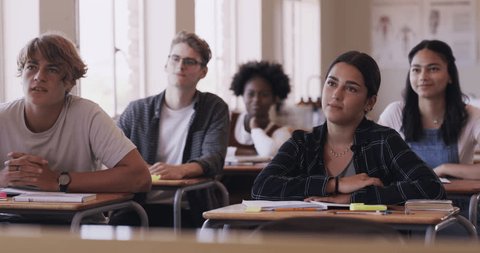 Education, learning and funny high school student group in a classroom sitting at a desk. Happy, teen and young adult students listening in class with a curious mind, smile and laugh ready to learn Video Stok