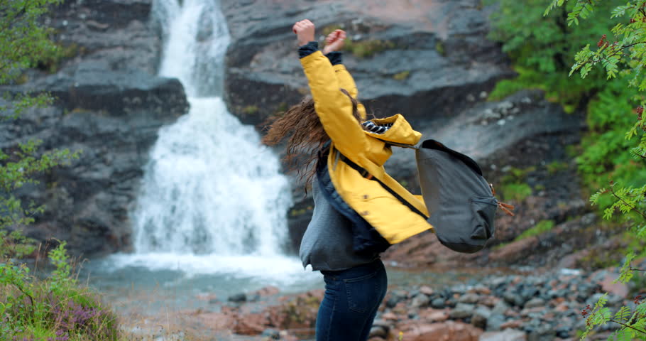 Hiking, travel and woman dance by waterfall in nature on vacation or trip. Carefree, freedom and happy female hiker having fun, dancing in rain and enjoying quality time alone on adventure by river. Royalty-Free Stock Footage #1100990333