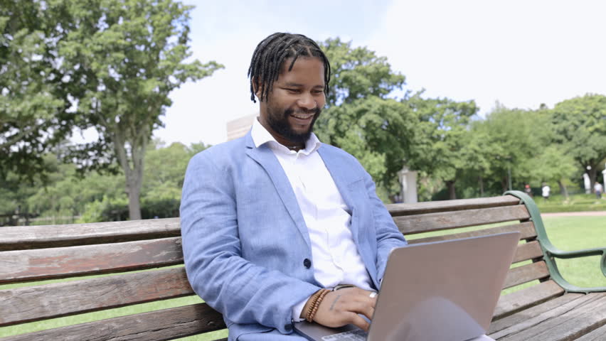 Business, black man on bench and in park with laptop, success and happiness with social media, typing and connection. Nigerian male employee, worker and entrepreneur with device, startup and smile