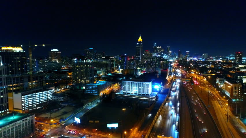 Aerial Backward Shot Of Cars Moving On Roads By Tall Buildings Against Clear Sky In Illuminated City - Atlanta, Georgia