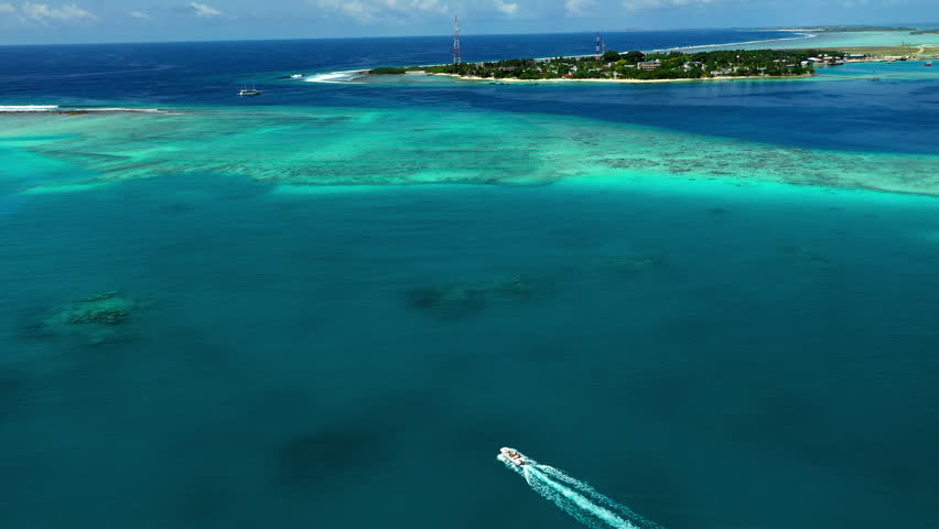 Aerial Shot Of Speedboat Moving By Island Under Clouds, Drone Flying Downwards Over Sea On Sunny Day - Thulusdhoo, Maldives