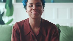 Young charismatic African American woman talks about himself by recording video resume for employers and boasts with smile about achievements at previous job sits in home interior. Camera view