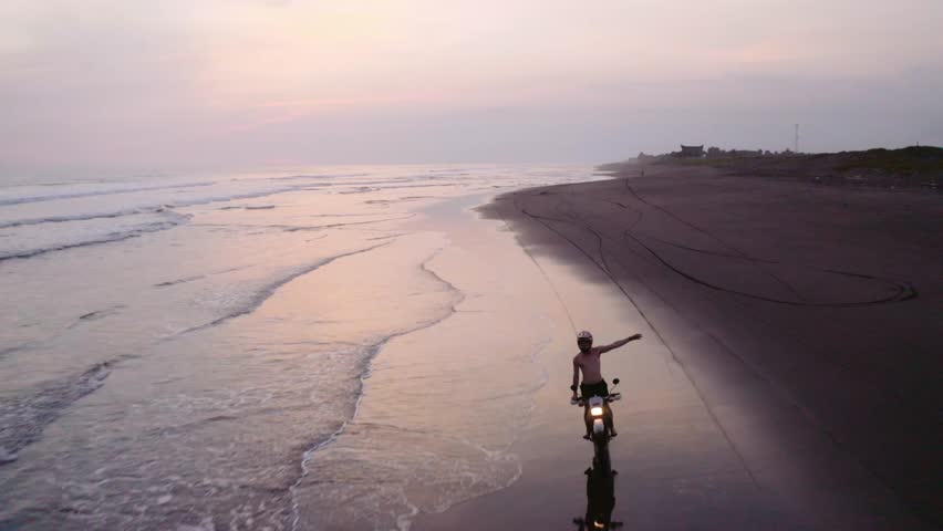 dirt bike rider loving life cruising along beach at sunset aerial reverse flight