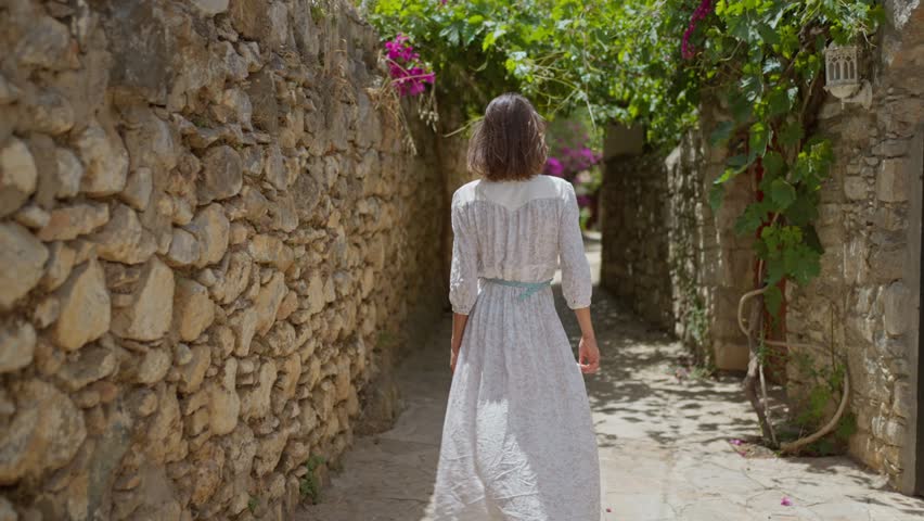 slow motion Smiling beautiful woman with flower wearing white dress walking street in old part of city enjoying vacation in Datcha, Turkey.