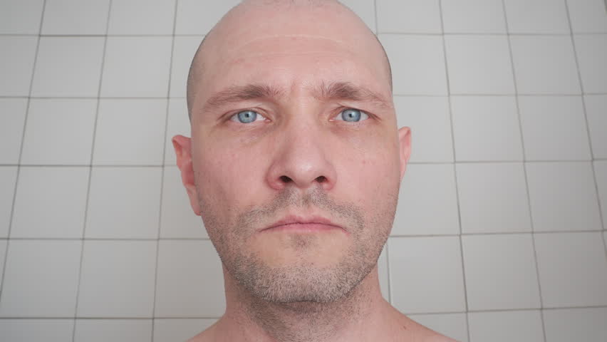 squinting eyes man looking close. male face eyeing something very close up. short-haired, unshaven man looks at camera very close, narrowing eyes against the background of white tiles in the bathroom. Royalty-Free Stock Footage #1101004865
