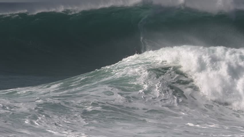 Surfer skillfully zigzags on a big wave that breaks behind him and ends his ride with a backflip