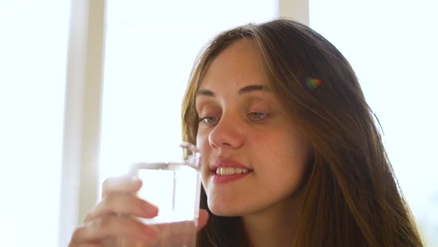 Young woman drinks fresh. girl drinks water from glass. Drinking water in glass. smiling girl holds transparent glass of water in her hand. girl drinks, quenches her thirst with sip of fresh water Royalty-Free Stock Footage #1101006097