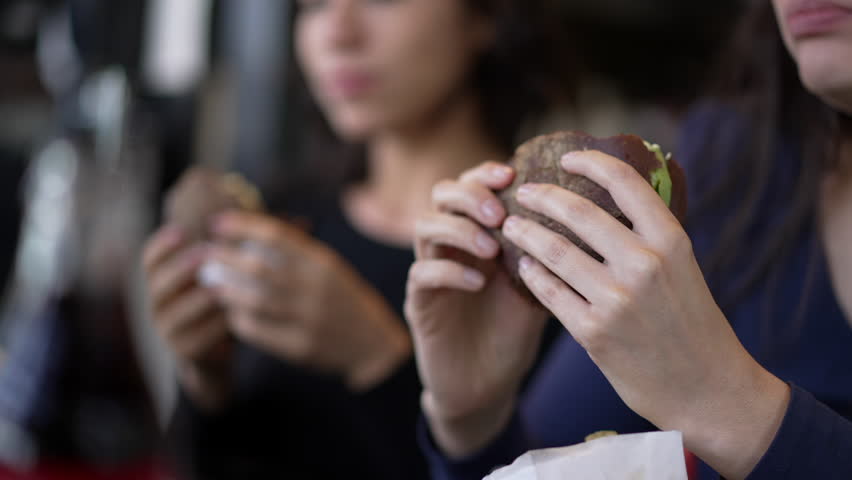 Closeup of female hands holding cheeseburgers. Two women about to take a bite of burgers