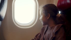 A charming girl is sitting at the window of the plane, the child looks out the window of the airplane during the flight. A teenage girl is flying in an airplane and is sitting by the window. 4K - Powered by Shutterstock - Get 15% off with code: PIKWIZARD15