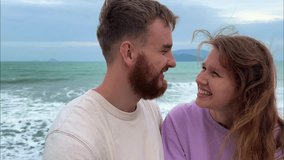 young happy couple in love on a honeymoon in bad weather, on vacation make a video selfie , sea background, the concept of a sweet relationship, kiss