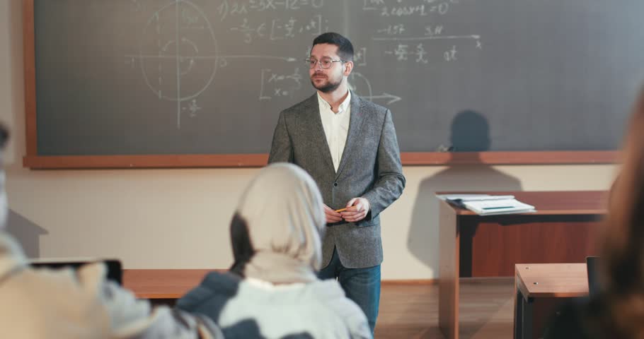 Caucasian male professor in glasses explaining material to students in classroom. Teaching concept. Man teacher at college talking at seminar. Teach and learn. Explanation at high school. | Shutterstock HD Video #1101012877