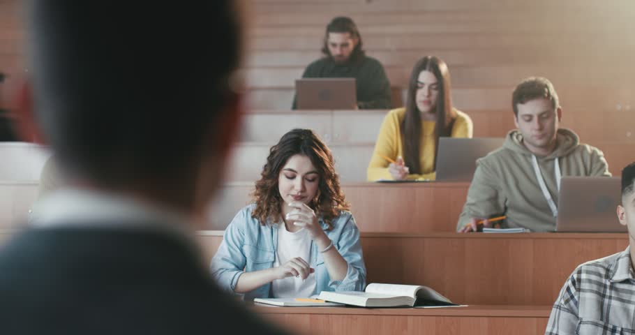 Caucasian young beautiful female student sitting at lection in University, rising hand and asking question or anwering to professor. Communiction between student and teacher. Girl talk with lecturer. Royalty-Free Stock Footage #1101012907
