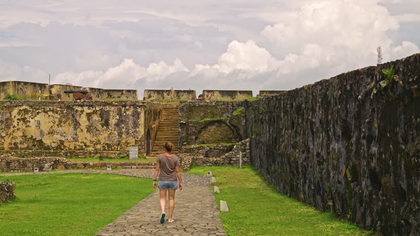 Female tourist looking at old Galle Dutch Fort walls covered in moss along a stone path in Sri Lanka