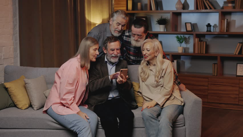 Group of Happy Senior Friends Using Smartphone Sitting on Sofa in Nursing Home. Mature Man Showing Something to His Friends, Scrolling Photos. Old People Spending Time Together. S3niorLife | Shutterstock HD Video #1101015403