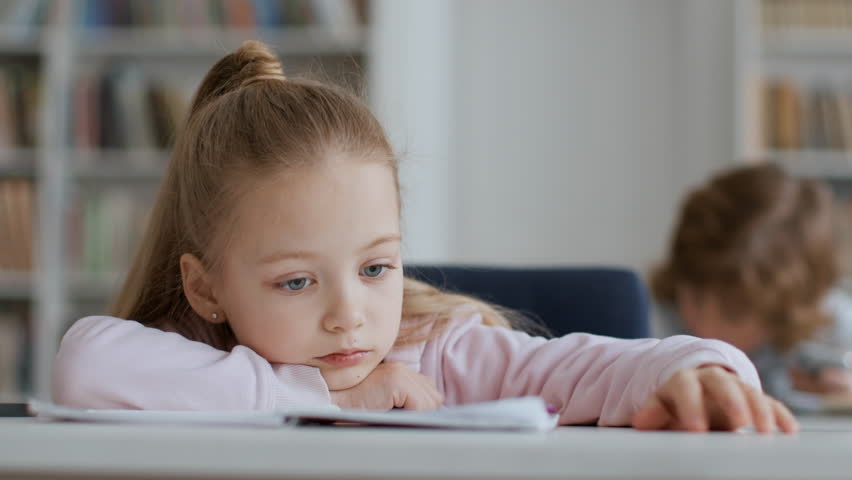 Bad mood at school. Close up portrait of upset little girl feeling boring during lessons, lying on desk and tapping fingers, free space Royalty-Free Stock Footage #1101017151