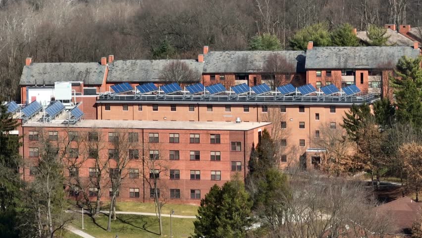 Solar panels on top of college dorms. Long aerial zoom shot of brick buildings with photovoltaic array on roof. Sustainable energy in winter theme. Royalty-Free Stock Footage #1101017629