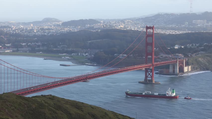 Cargo ship with tug sails under Golden Gate Bridge to port in San Francisco Bay