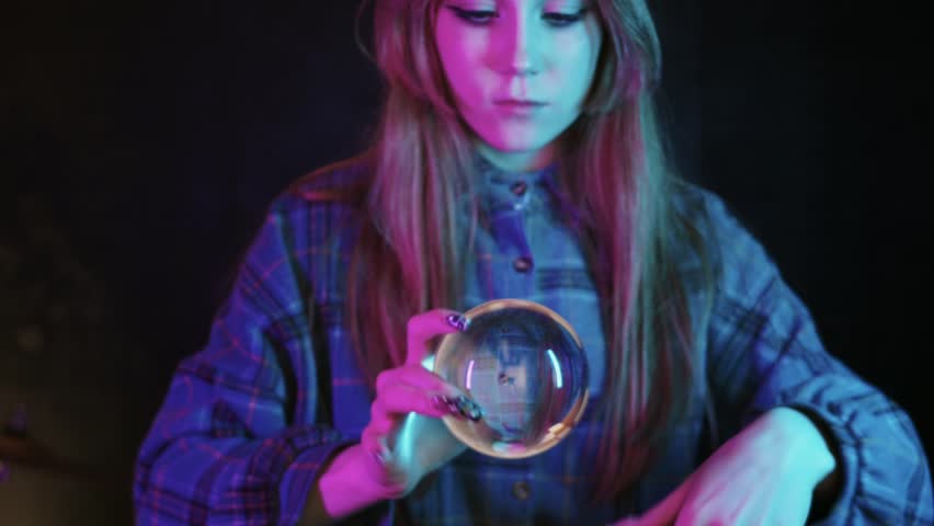 A young woman does contact juggling with crystal ball in pink lighting