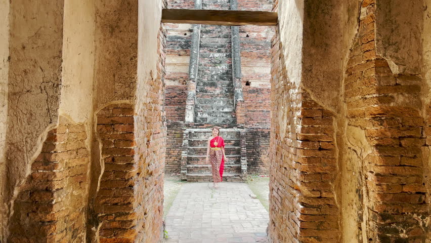 young woman wearing traditional red Thai dress and golden accessories walk in the historical site Wat Chaiwatthanaram temple. Thai national costume