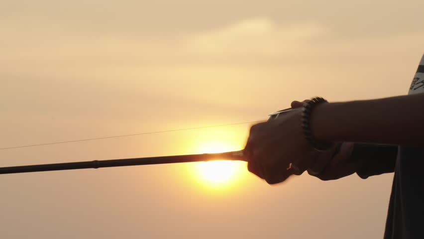boy holding outside fishing rod fishing at the reservoir at Sunset time silhouette