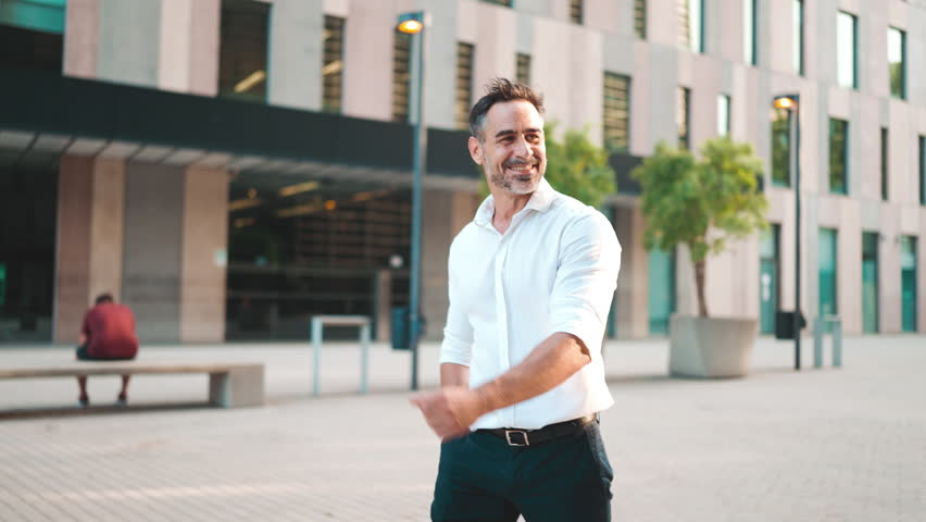Emotional smiling Mature businessman with neat beard wearing white shirt is walking on the street of modern city. Successful man relaxed, enjoying life Royalty-Free Stock Footage #1101027317