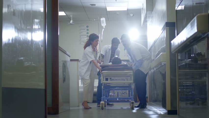 A rapid response team of doctors and nurses running or rushing a critical patient on a stretcher trolley to an operation theatre or medical emergency unit or ICU in a modern hospital corridor. 