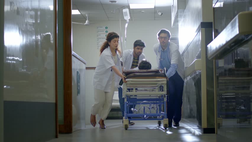 A rapid response team of doctors and nurses running or rushing a critical patient on a stretcher trolley to an operation theatre or medical emergency unit or ICU in a modern hospital corridor. 