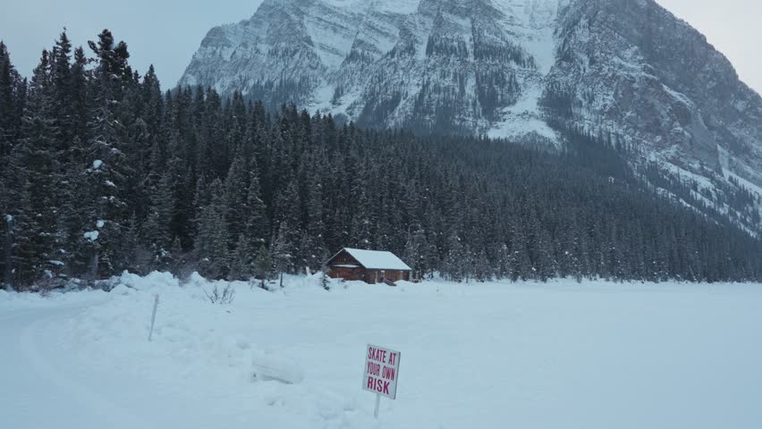Beautiful scenery of Lake Louise with wooden cottage glowing and rocky mountains with snowfall in winter at Banff national park, Alberta, Canada