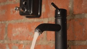 water flows from a black tap against a brick wall. man turned off the tap with water. High quality Full HD video recording