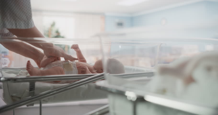 Attentive Mother Changing Diaper to a Newborn Baby. Neonate Child Lying in a Hospital Crib in a Nursery Clinic Facility. Motherhood, Childhood and Medical Concept Royalty-Free Stock Footage #1101035609
