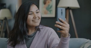 Portrait of cheerful Asian girl making online video call with smartphone showing thumbs-up indoors at home. Communication and people concept.